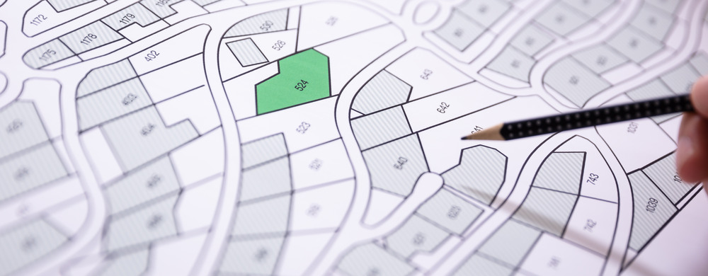 Close-up Of Human Hand Holding Pencil Over Paper Cadastre Map