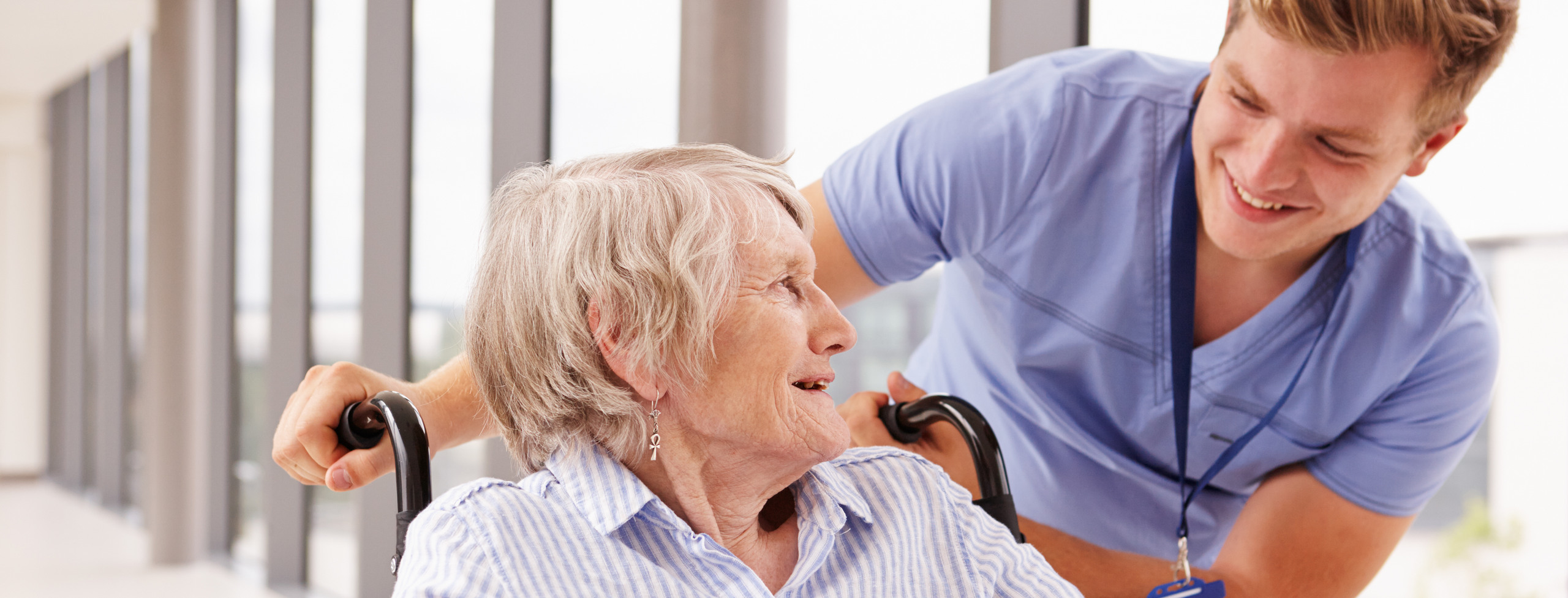 En äldre rullstolsburen kvinna som ler mot omsorgspersonal som står bakom henne