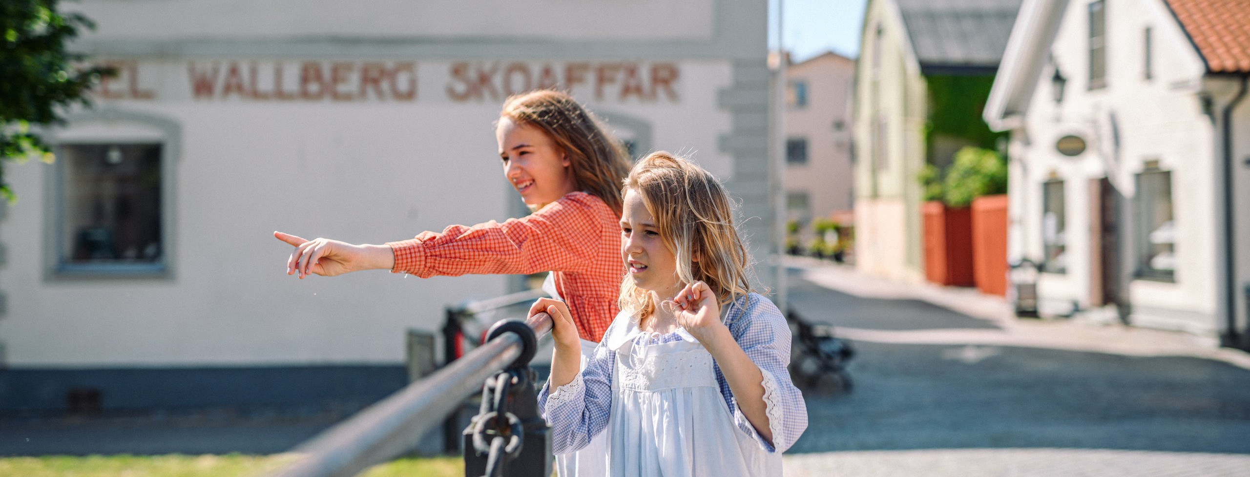 Foto: Två flickor står på en kullerstensgata vid en bro och pekar ut mot vattnet.