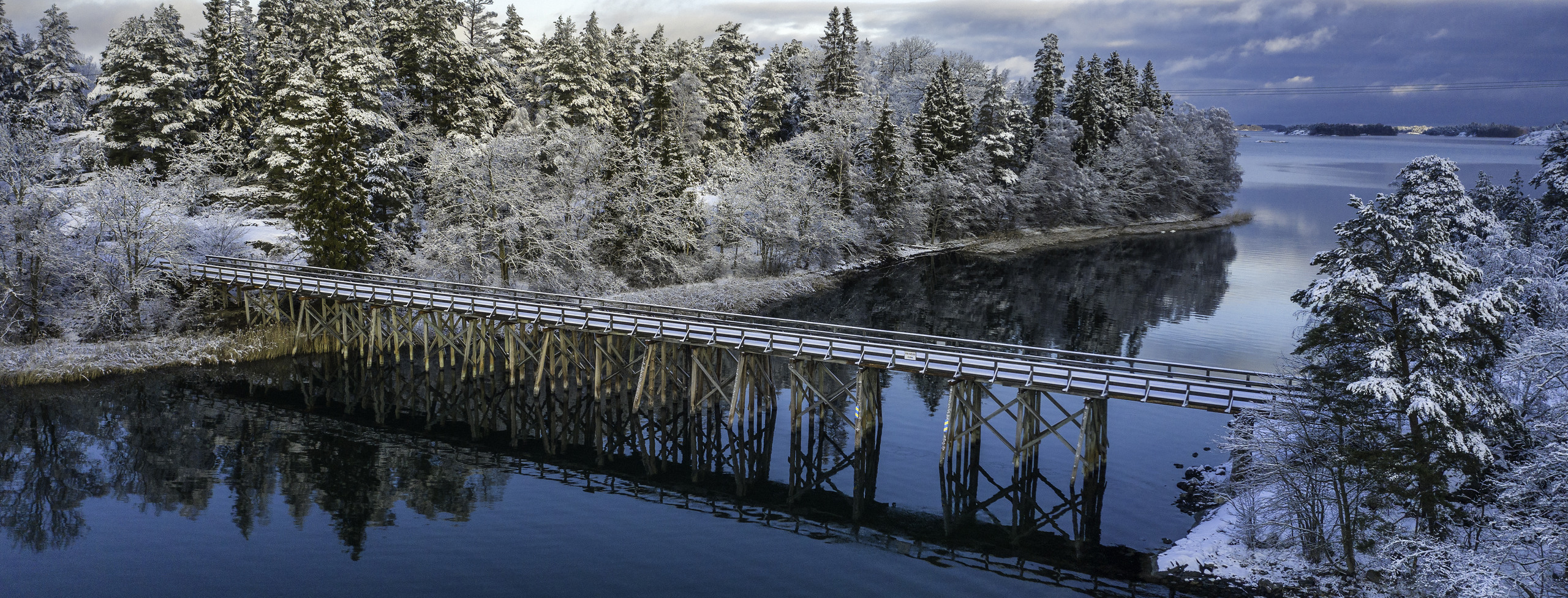 Bild visar en träbro mellan två öar  vintertid i Sankt Annas skärgård.