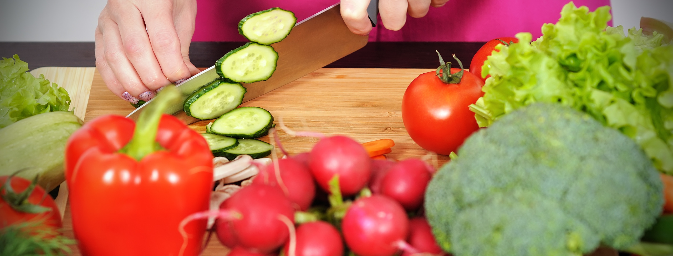 Bild visar olika grönsaker framför en skärbräda och en person som skär upp gurka