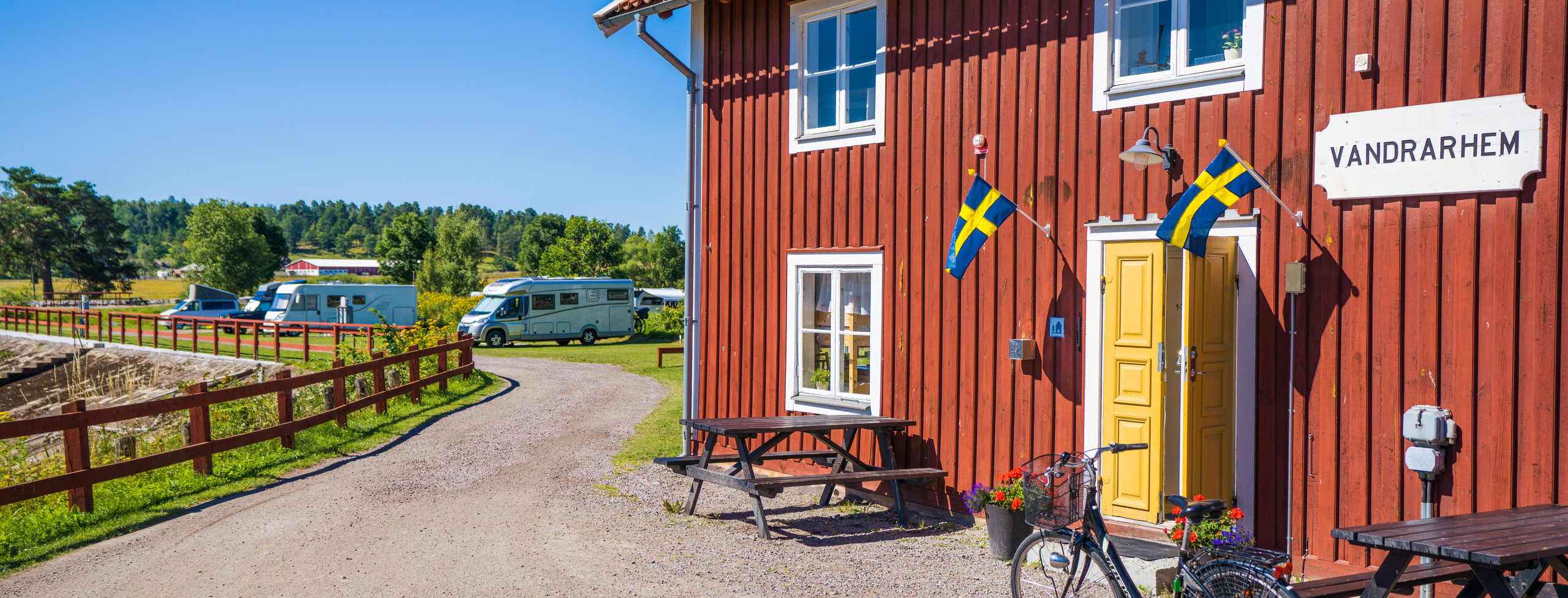 Foto: Bild visar Skeppsdockans camping. Ett rött hus med vandrarhem i förgrunder och husbilar i bakgrunden