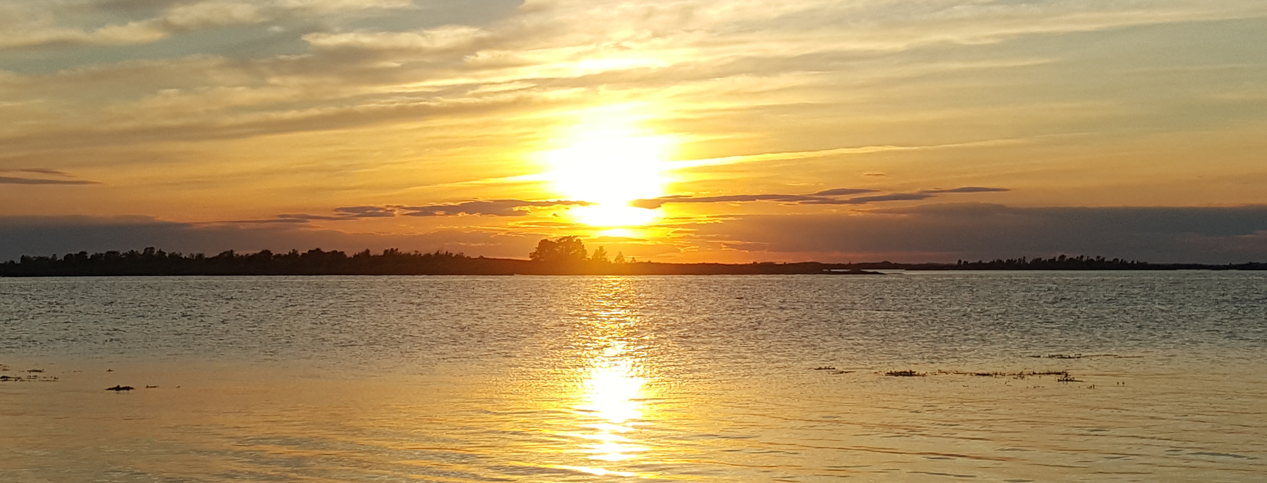 Solnedgång över skärgården. Solen speglar sig i vattnet.