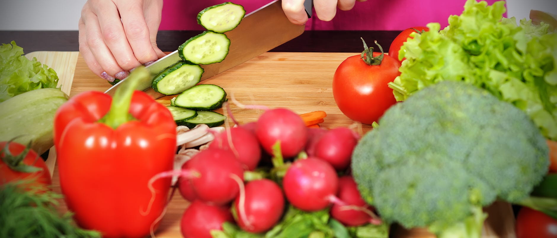 Bild visar olika grönsaker framför en skärbräda och en persom som skär upp gurka