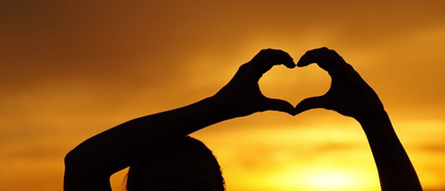 En person som håller sina händer i form av ett hjärta i solnedgång
