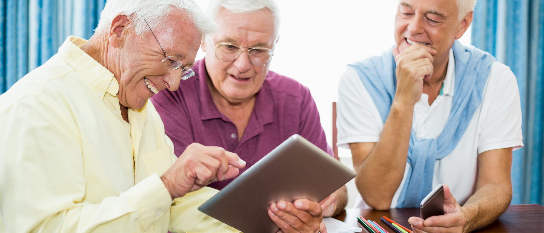 tre äldre herrar som sitter med en digital läsplatta och pekar och läser