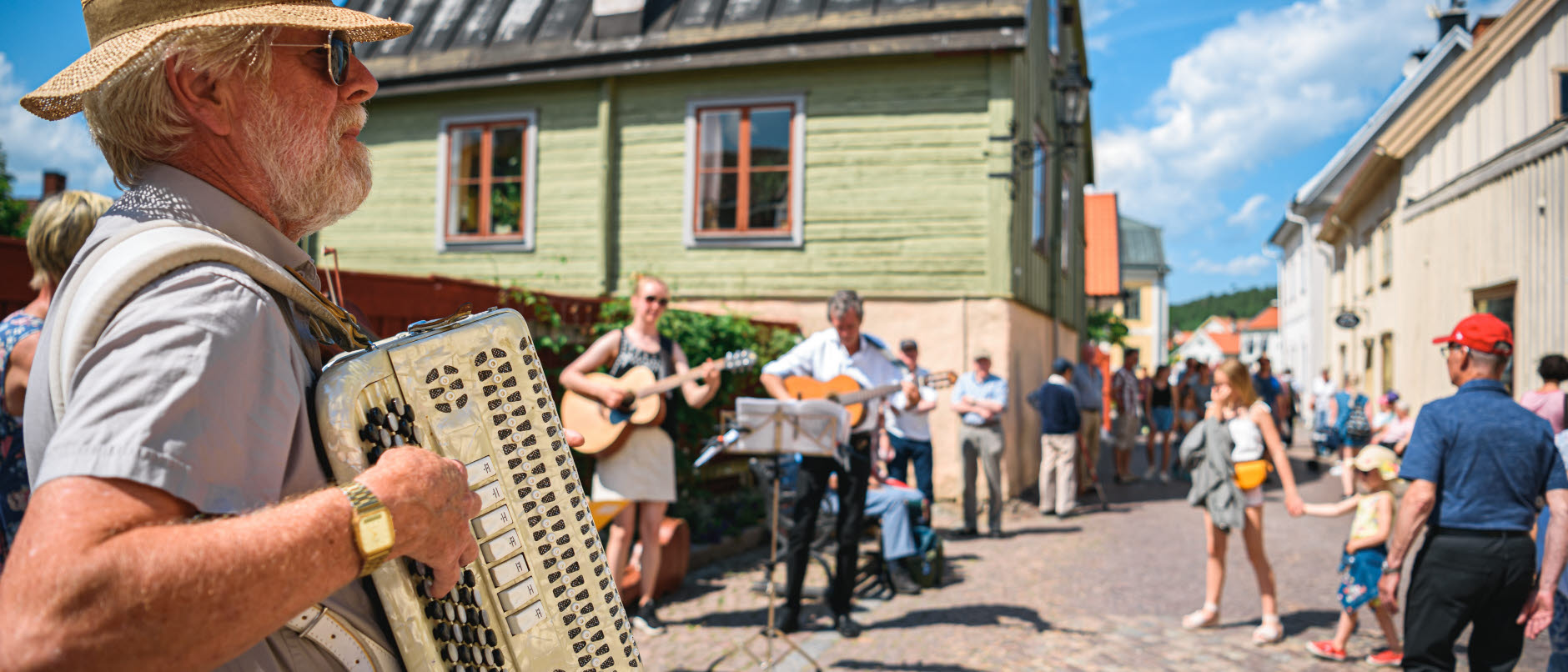 Foto: Bild visar en man som spelar dragspel i förgrunden bakom syns Storgatan med kullestenar och medeltida hus. Det spelas musik och människor ser på.